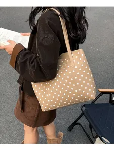 Una donna porta una borsa beige a pois bianchi con tracolla lunga mentre tiene un libro
