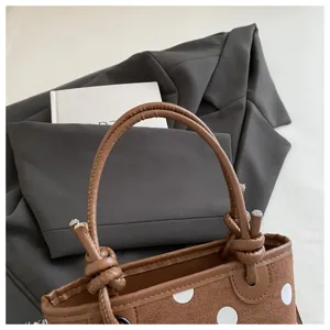 Dettaglio di una borsa marrone effetto scamosciato, a pois bianchi, con manici annodati e cuciture decorative