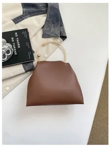 Borsa marrone con manico ad anello dorato, esposta su una superficie bianca accanto a libri e abiti