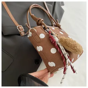 Primo piano di una borsa marrone effetto scamosciato a pois bianchi, con manici e ciondoli decorativi