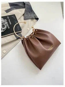 Dettaglio di una borsa marrone arricciata, con manico curvo dorato e anello metallico