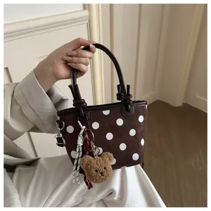 Dettaglio di una borsa marrone a pois bianchi, con ciondolo a orsetto e nappa intrecciata