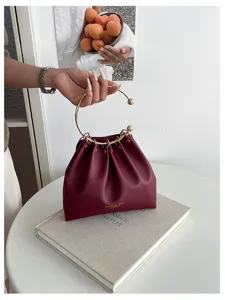 Borsa bordeaux arricciata con manico ad anello dorato, appoggiata su un libro e tenuta a mano