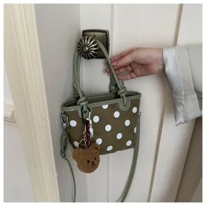 Borsa verde oliva a pois bianchi appesa alla porta, con manici annodati e ciondolo di orsetto
