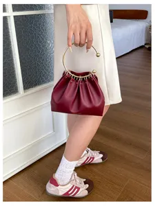 Borsa bordeaux plissettata con manico ad anello dorato, portata da una modella in una stanza luminosa