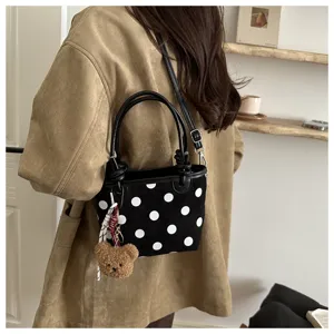 Donna con una piccola borsa nera effetto camoscio a pois bianchi e ciondolo a forma di orsetto.
