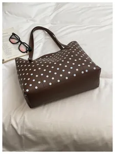 Borsa marrone a pois bianchi con manici lunghi, distesa su biancheria da letto bianca