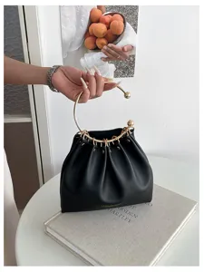 Borsa nera arricciata con manico ad anello dorato, mostrata su un libro e tenuta a mano