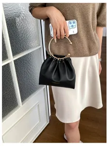Una persona tiene una borsa a secchiello nera arricciata, con manico ad anello dorato, al chiuso.