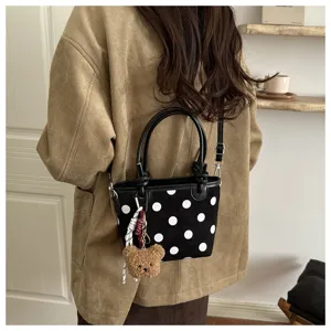 Vista da dietro: donna con borsa nera a pois bianchi, ciondolo a orsetto e tracolla lunga