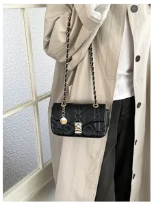 Borsa nera trapuntata indossata con un trench beige, con catena dorata intrecciata e ciondolo.