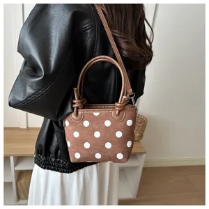 Borsa marrone a pois bianchi, con manici effetto pelle e tracolla, indossata sopra una gonna bianca