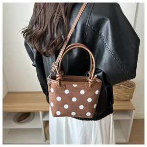Primo piano di una piccola borsa marrone a pois bianchi, con manici intrecciati, indossata a spalla