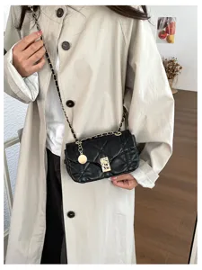 Dettaglio di una borsa nera trapuntata con patta e catena dorata, indossata sopra un cappotto beige