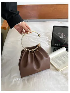 Borsa marrone in similpelle arricciata, tenuta per il manico ad anello dorato in camera