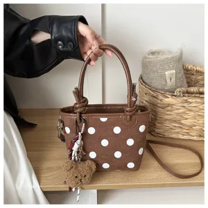 Dettaglio di una borsa marrone a pois bianchi, con manici effetto pelle e un ciondolo a forma di orsetto