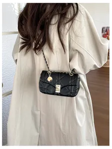 Borsa nera trapuntata con catena dorata e ciondolo sopra un cappotto beige, vista da dietro