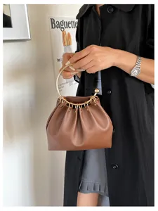 Una persona tiene una borsa marrone arricciata, con manico circolare dorato e borchie decorative.