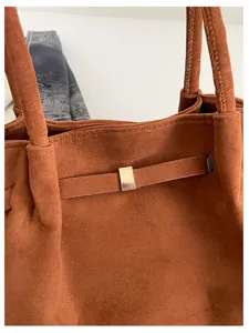 Close-up showing the brown suede-like surface, stitched handles, and small metal buckle detail