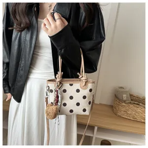 Una donna porta borsa crema a pois, manici intrecciati, ciondolo orsetto e catena con nappa