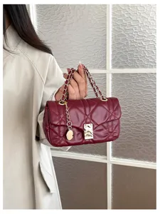 Dettaglio di una borsa trapuntata bordeaux tenuta in mano, con catena e chiusura dorate