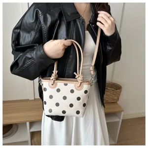Una modella tiene una borsa color crema a pois marroni, con manici e tracolla color beige