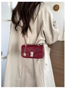 Borsa bordeaux trapuntata con catena e chiusura dorate, indossata sopra un trench color crema
