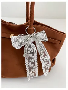 Close-up of a brown suede-look bag with a white lace bow, pearl trim and silver ring