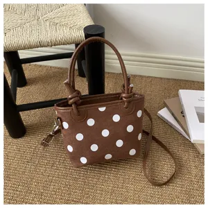 Borsa marrone a pois bianchi con manici in pelle, esposta su un tappeto intrecciato accanto a libri