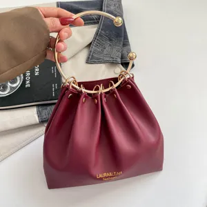 Dettaglio di una borsa bordeaux arricciata, con manico ad anello dorato e borchie decorative