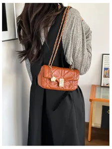 Una donna indossa una borsa marrone trapuntata, con tracolla a catena dorata e ciondoli metallici