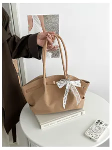 Tan handbag with long handles, white lace bow and pearl accents, held above a round table