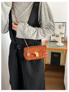 La modella indossa una borsa trapuntata arancio-bruna con catena dorata e ciondoli metallici.