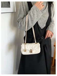 Borsa bianca trapuntata con catena e chiusura dorate, indossata con un outfit casual in un interno