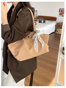 Side view of a model carrying a tan suede-textured tote with a white lace bow and metal ring charm