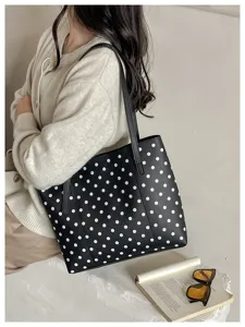 Borsa nera a pois bianchi portata a spalla, accanto a un libro aperto e agli occhiali da sole
