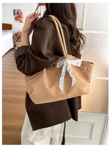 Woman wearing a tan tote with a white lace bow charm, shown over the shoulder in a bright room