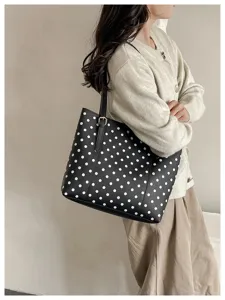 Una donna porta a spalla una borsa nera a pois bianchi, con dettagli dorati e una tracolla sottile