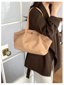A model wears a soft camel suede-look bag with slim handles and metal accents over a brown coat