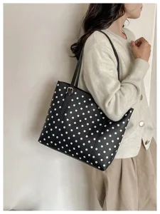 Una donna porta una borsa nera a pois bianchi, con manici sottili e dettagli metallici dorati.