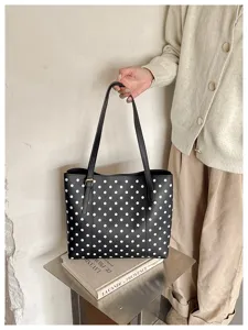 Modella con una borsa nera a pois bianchi, doppi manici lunghi e dettagli color oro