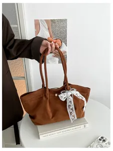 Brown suede-textured tote held by its handles, with a lace ribbon, pearl accents and metal rings