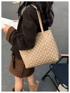 Vista all’aperto di una borsa beige a pois bianchi portata a spalla in una scena di strada