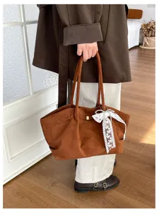 Close-up of a brown suede-texture tote with lace bow and gold buckle, carried by hand indoors