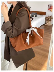 Side view of a woman carrying a soft brown suede-look tote with a white lace bow and pearl strands