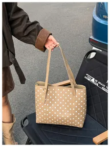Vista all'aperto di una borsa beige a pois bianchi, tenuta per i lunghi manici in una scena urbana
