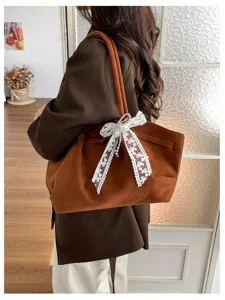 Lifestyle view of a brown suede tote carried on the shoulder, with a white lace bow and rhinestones