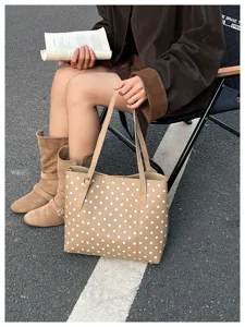 Borsa color cammello a pois bianchi accanto a una persona seduta che legge su una sedia pieghevole
