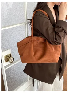 Model carries a brown suede-look tote over one shoulder, with slim handles and a metal clasp.