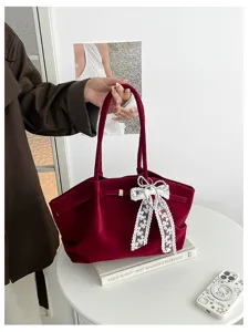 Burgundy velvet tote with a white lace bow, held by its handles above a round white table
